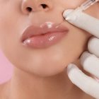 Young woman getting lips injection on pink background, closeup